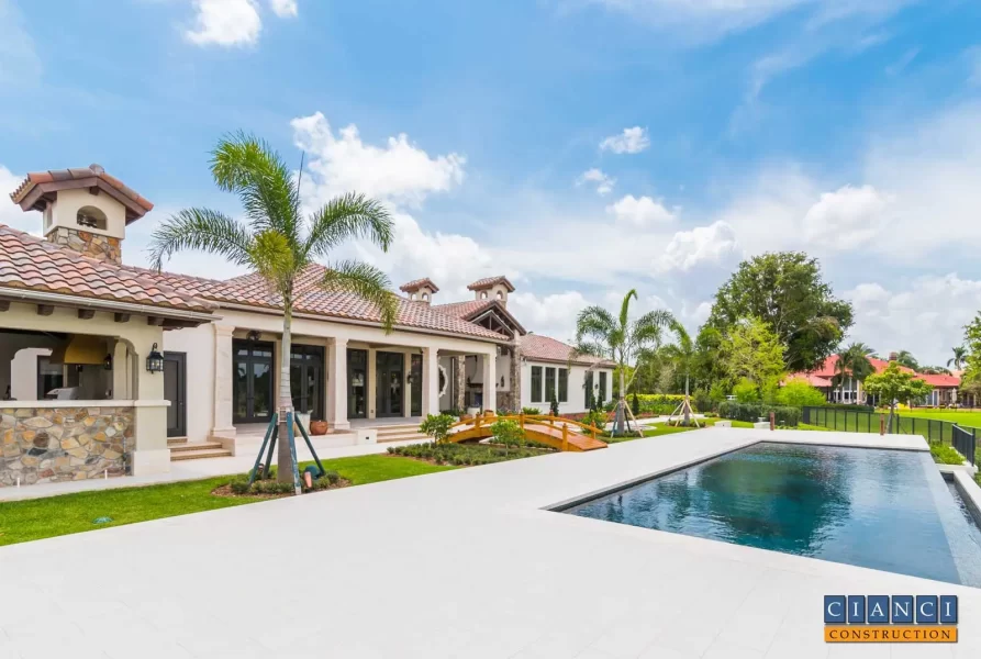 Simple clean lines of Custom Country Tuscan styled home with view of vanishing edge pool and arched wood step bridge